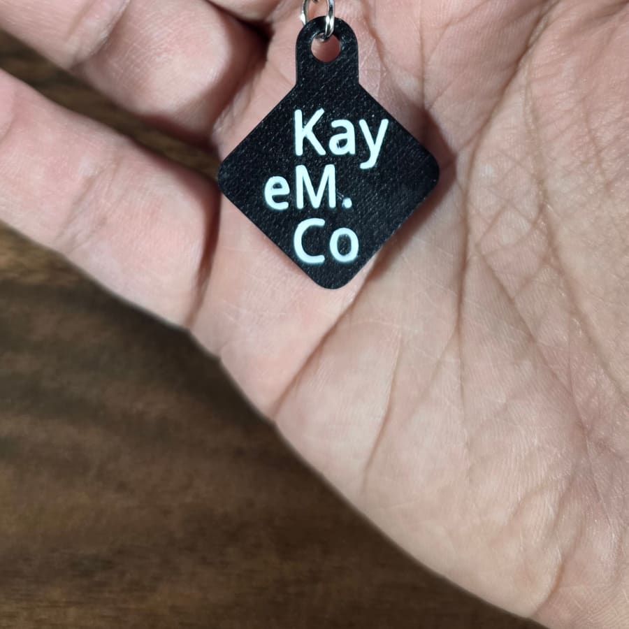 Black KayEmCo keychain tag held in a hand