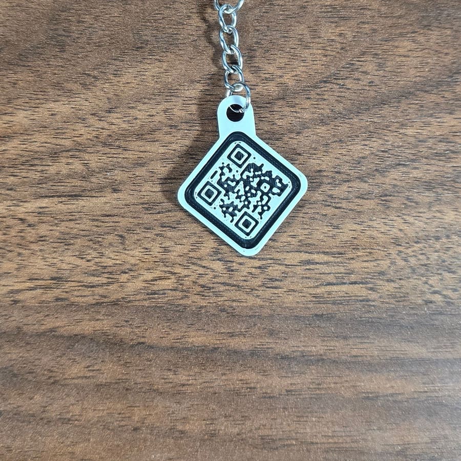 White QR code keychain with silver chain on a wood table
