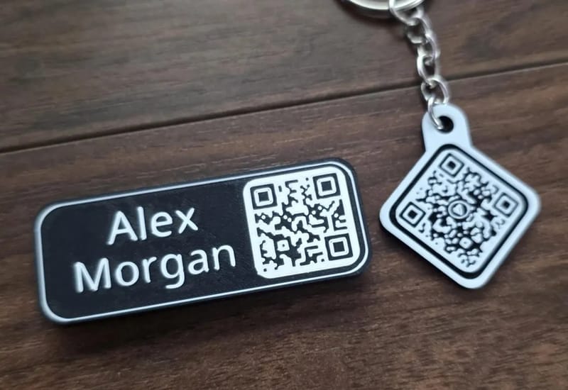 Kayem.co name tag with an engraved name and QR code next to a matching QR keychain on a wood table